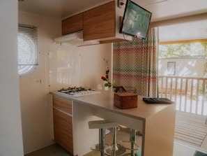 A compact kitchen with a gas stove, wooden cabinets, a small bar area with stools, and a television mounted above the counter.