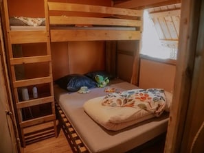 Een stapelbed met een onderste bed, een ladder, een klein plankje en een raam.