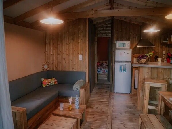 A cozy cabin interior with a sofa, wooden flooring, a kitchen area, and a hallway leading to a bedroom.