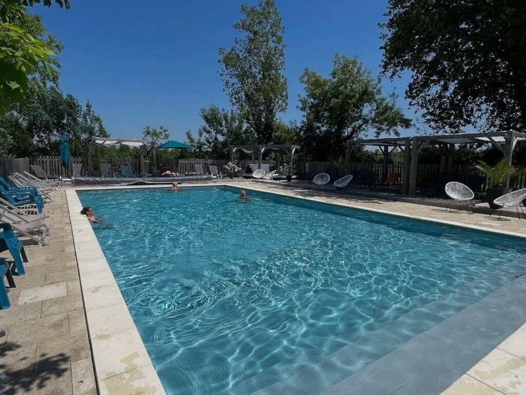 Una piscina rectangular con agua cristalina y azul, rodeada de sillas de descanso y sombrillas.