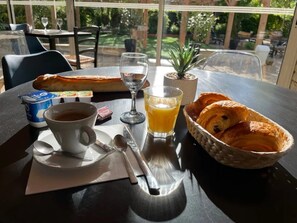 Una mesa con alimentos para el desayuno, como cruasanes, una taza de café, un vaso de zumo de naranja y una pequeña planta.