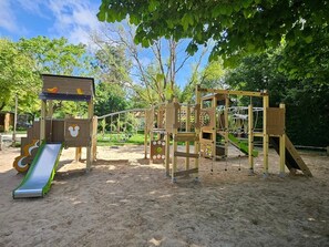 Un parque infantil con un tobogán, estructuras para escalar y una casita de madera.