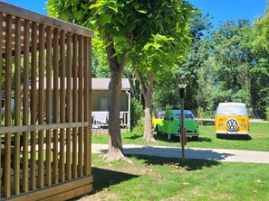 A wooden fence, a green and yellow vehicle, and a yellow van parked in a grassy area with trees and a building in the background. - Chalet 4 étoiles - Piscine  - eehefh (Coulon)