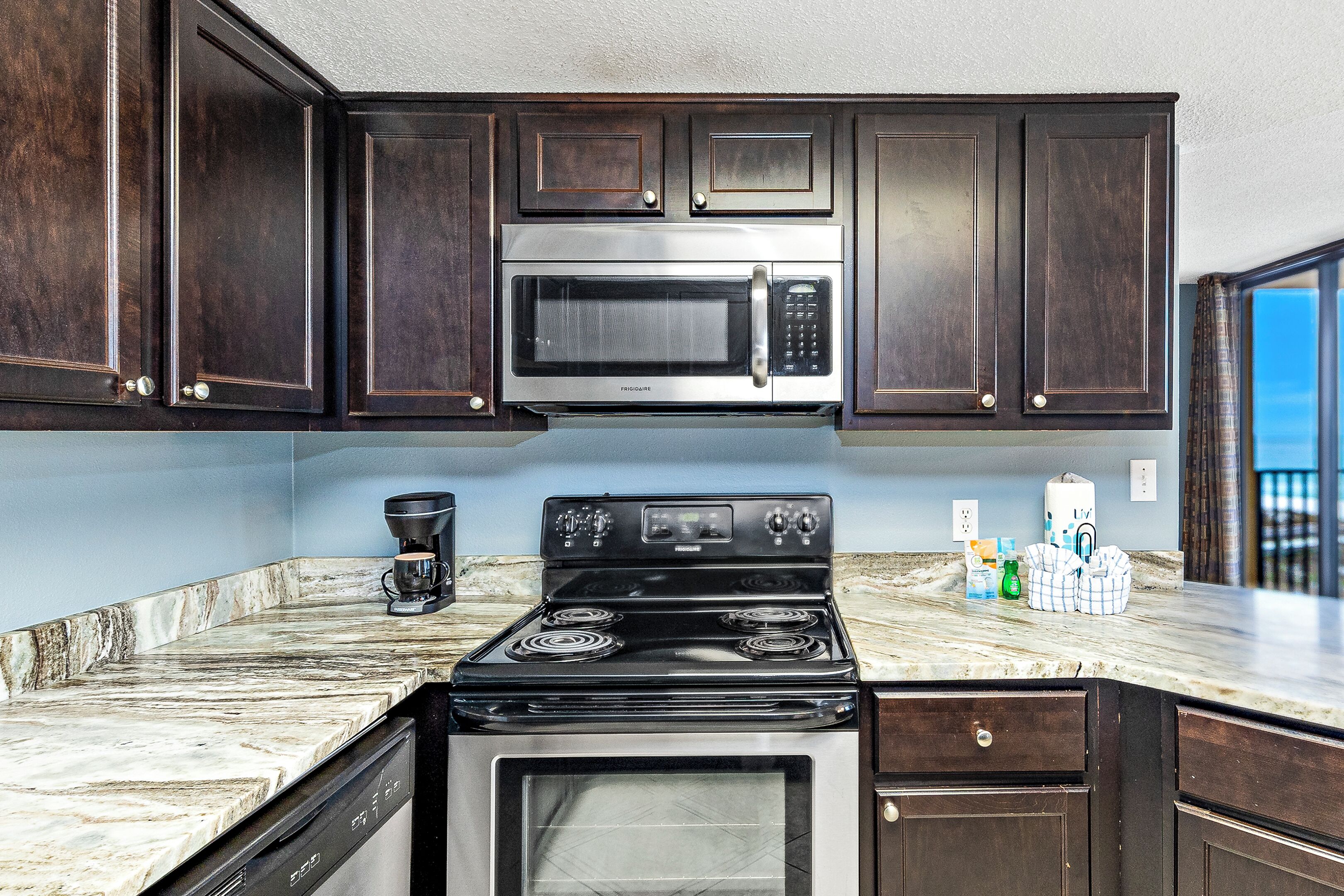 A kitchen with dark wood cabinets, a stainless steel microwave, a black stove, and a marble countertop.