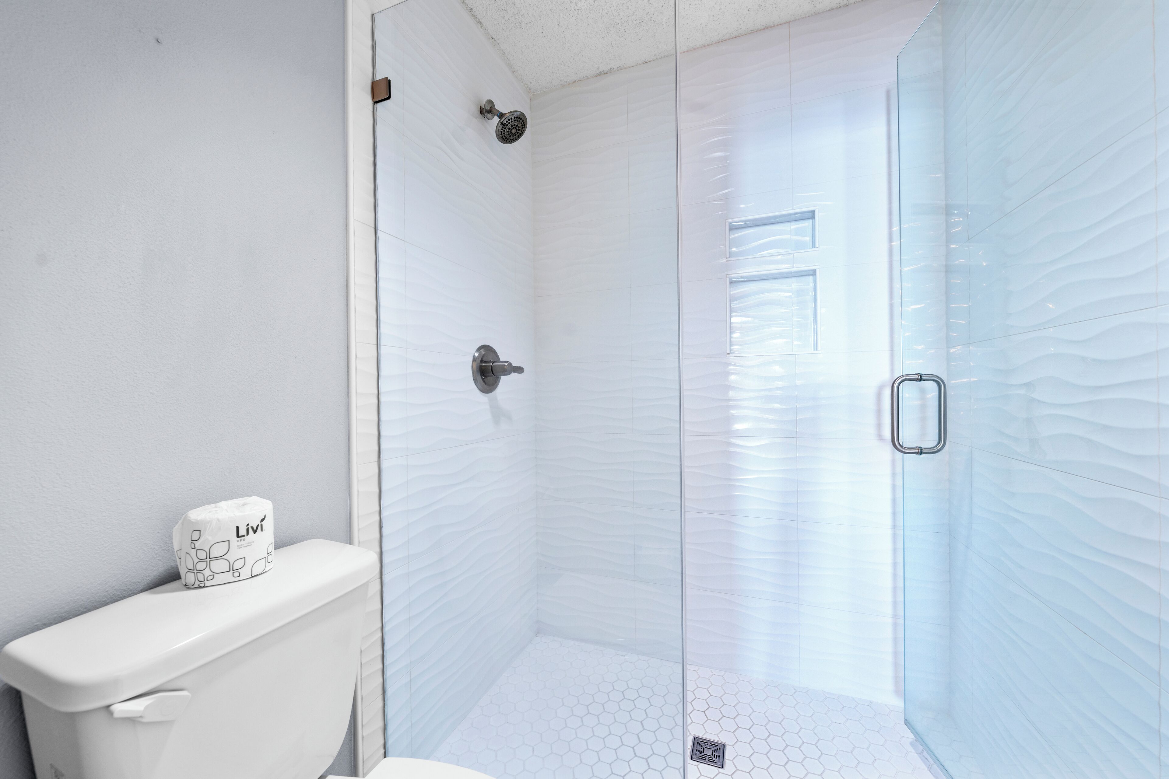 Une salle de bain avec des toilettes, une douche dotée d’une porte en verre et un sol carrelé de motifs hexagonaux.