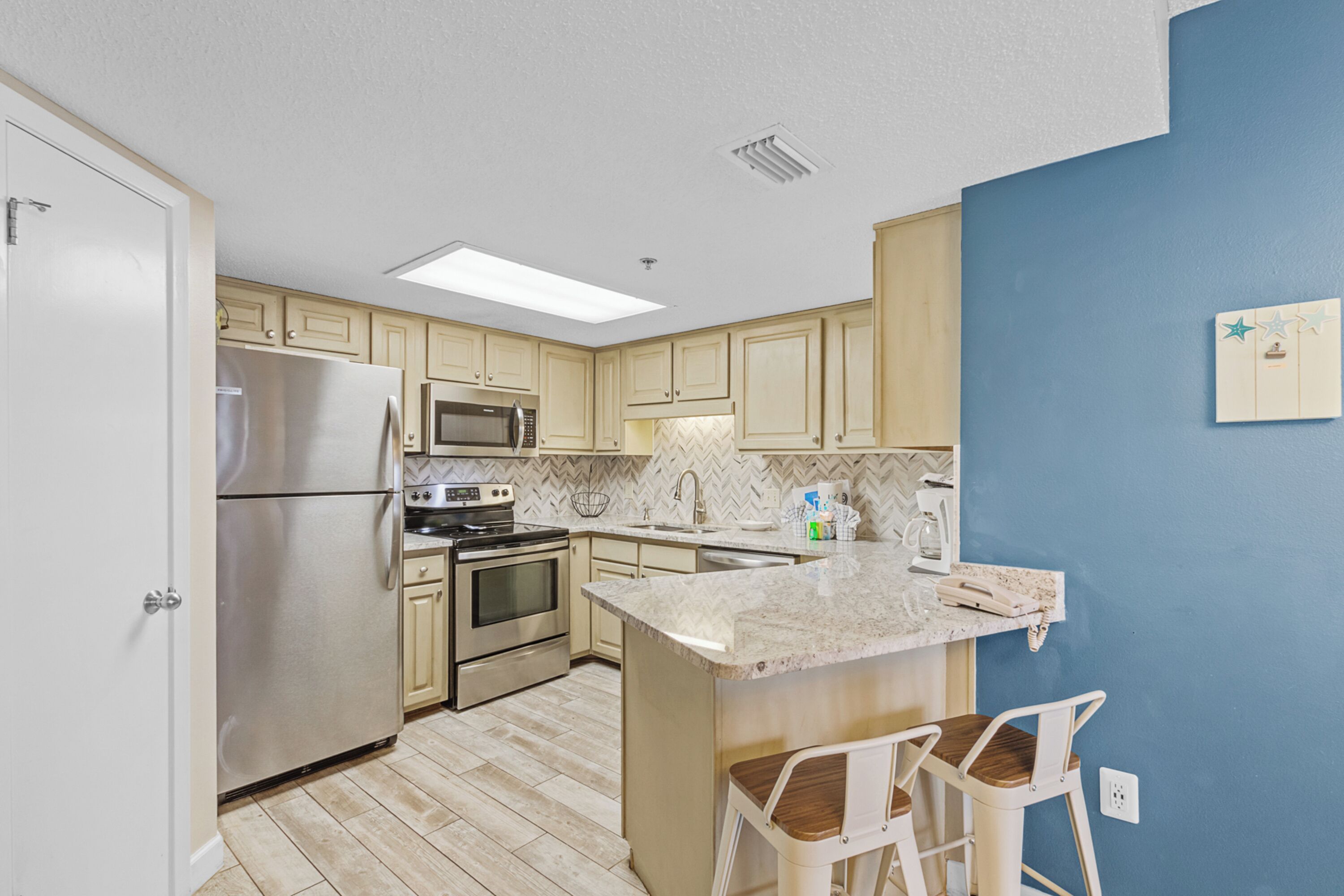 Una cocina moderna con armarios de madera clara, electrodomésticos de acero inoxidable, encimera de mármol y una pared de acento azul.