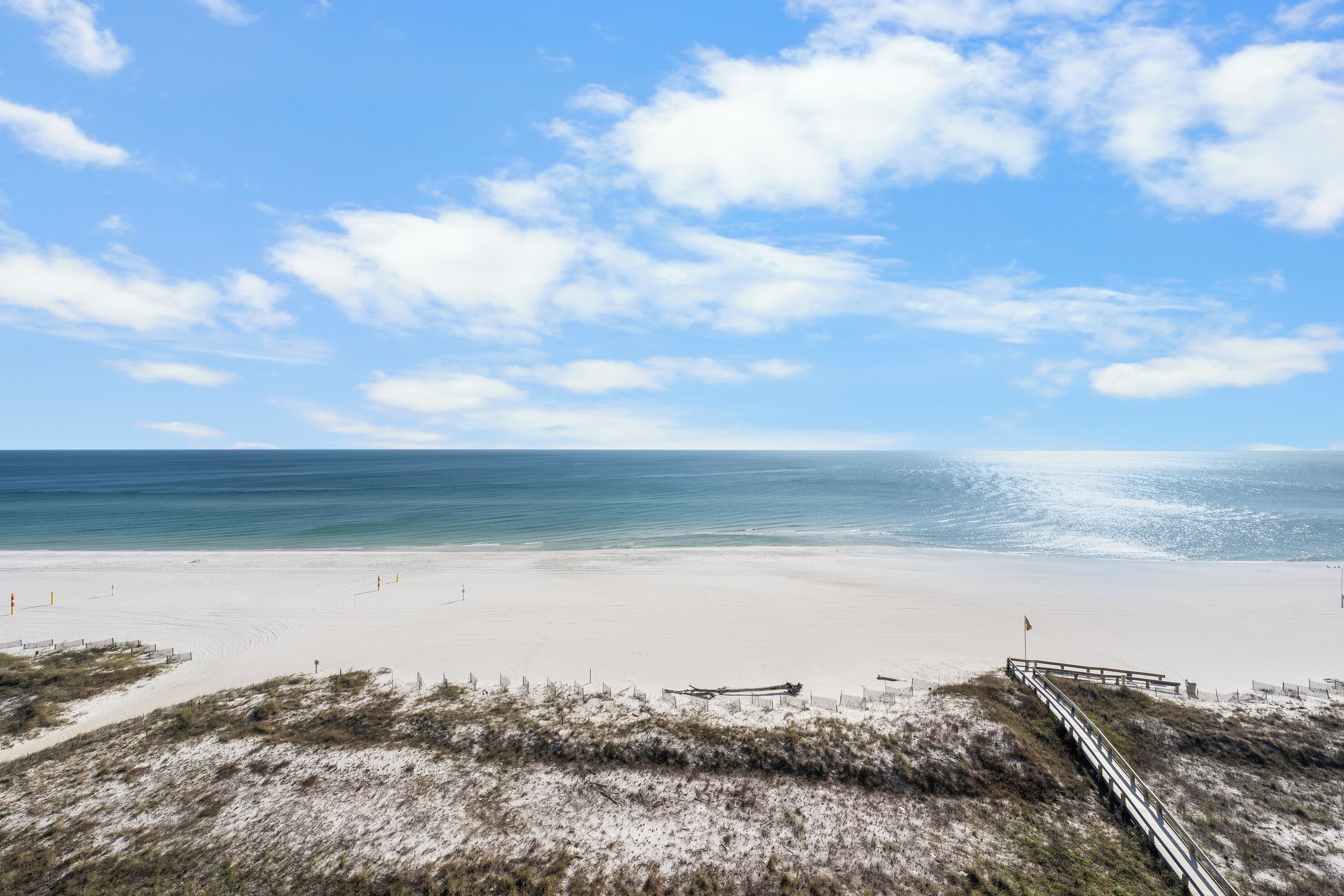 A beach with a wooden walkway leading to the water, a sandy shore, and a clear sky.