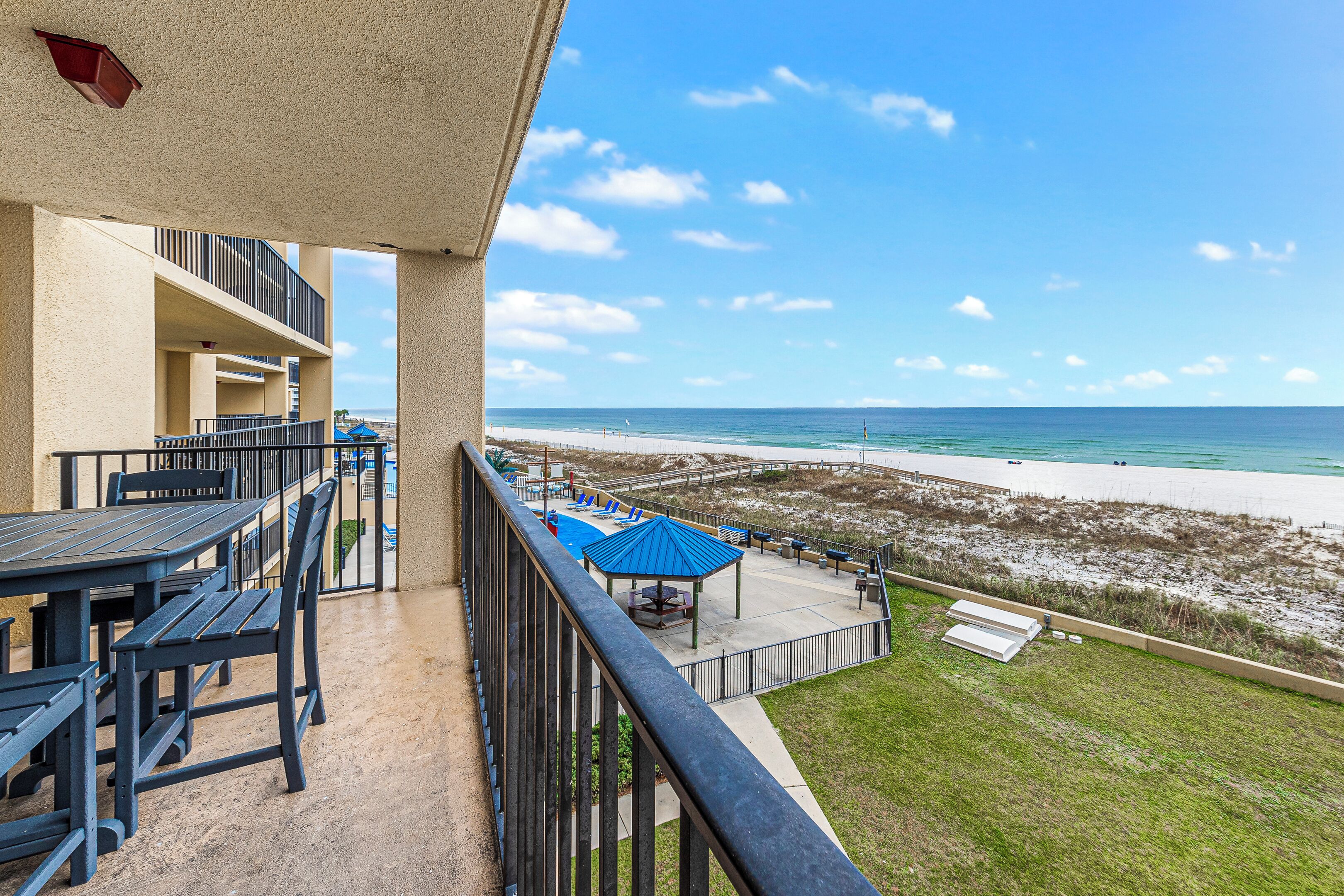A balcony with a view of the beach, outdoor seating, and a covered area.