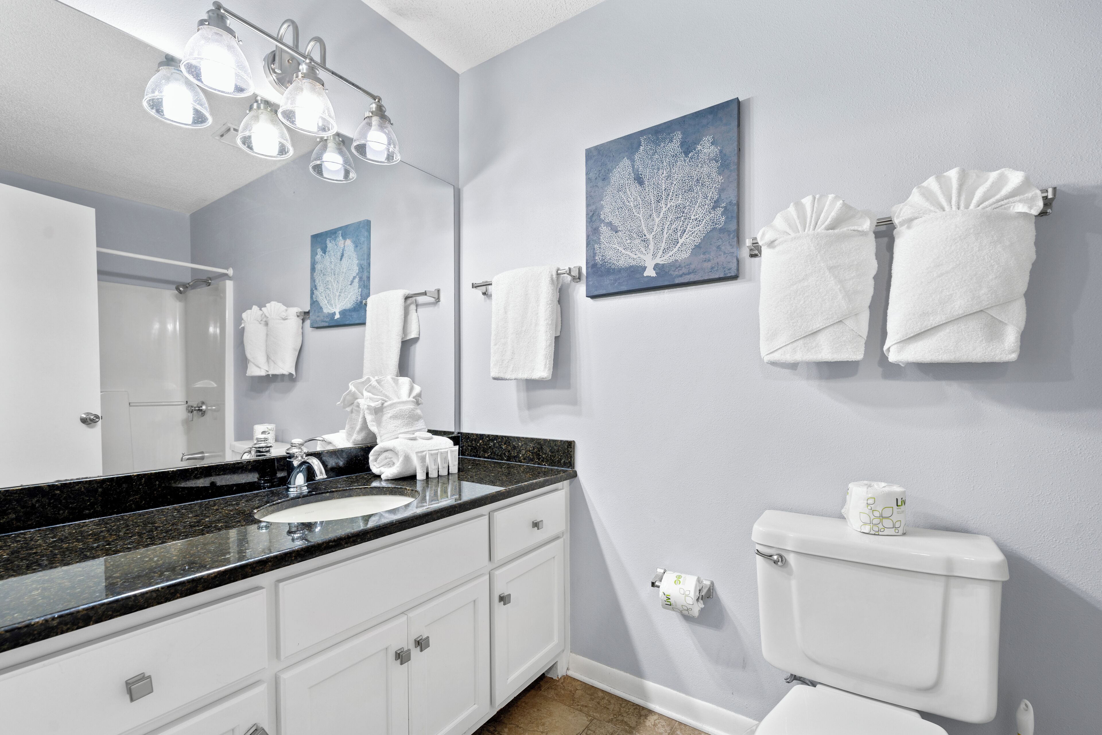 A bathroom with a black granite countertop, white cabinets, a white toilet, and two towels hanging on the wall.