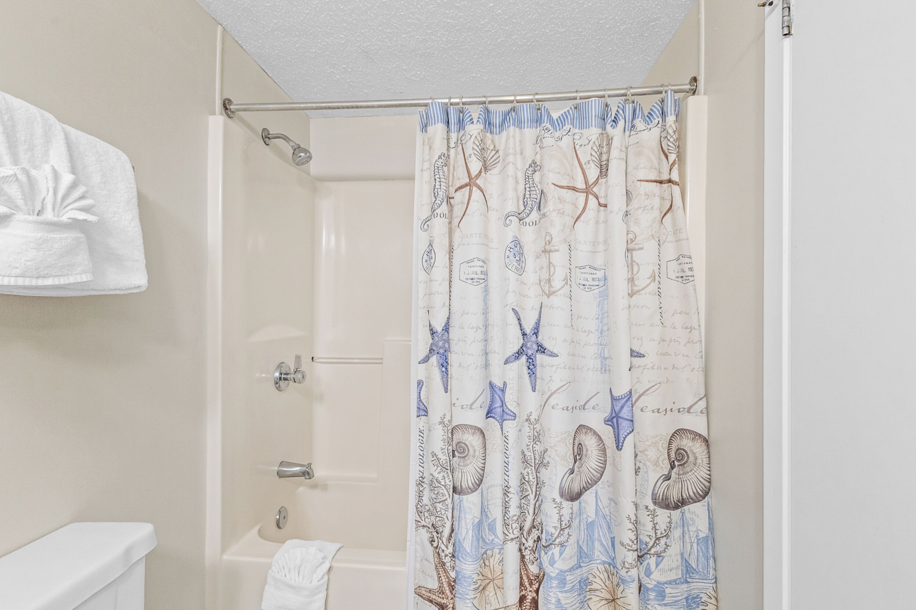 A bathroom with a shower curtain featuring sea creatures and script patterns, a white towel hanging on the wall, and a bathtub.