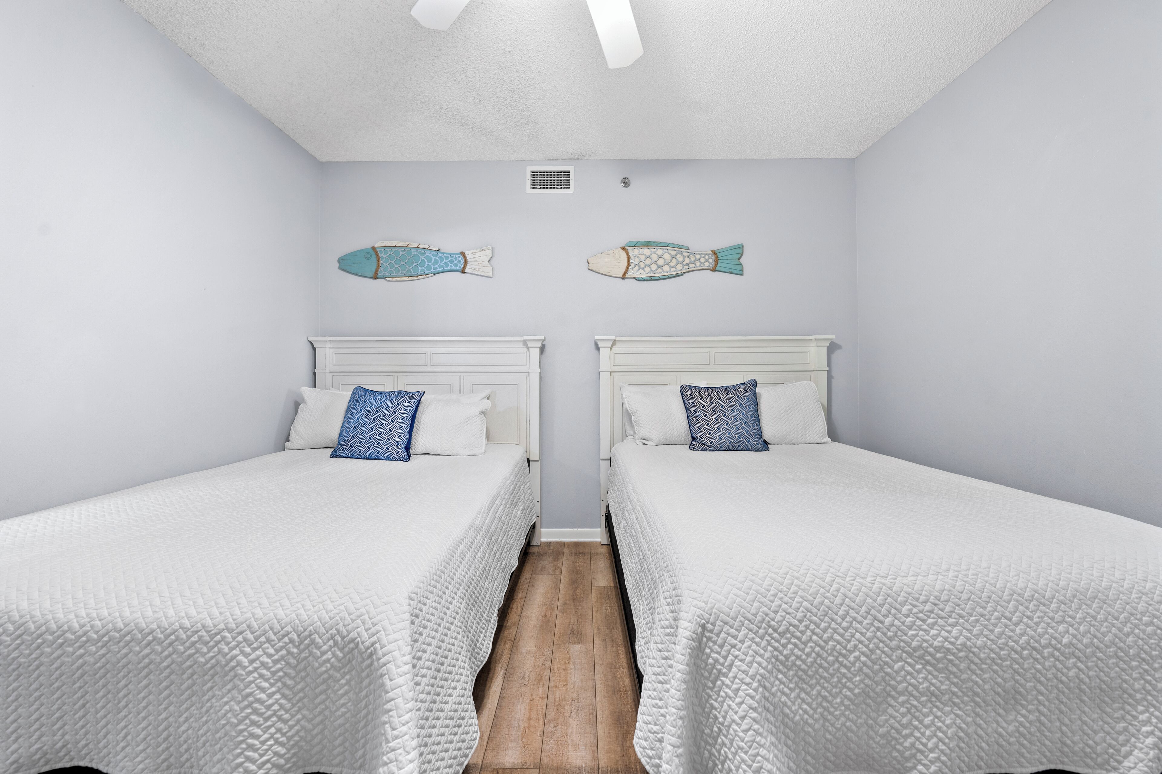 Une chambre avec deux lits, du linge de lit blanc et un plancher en bois.