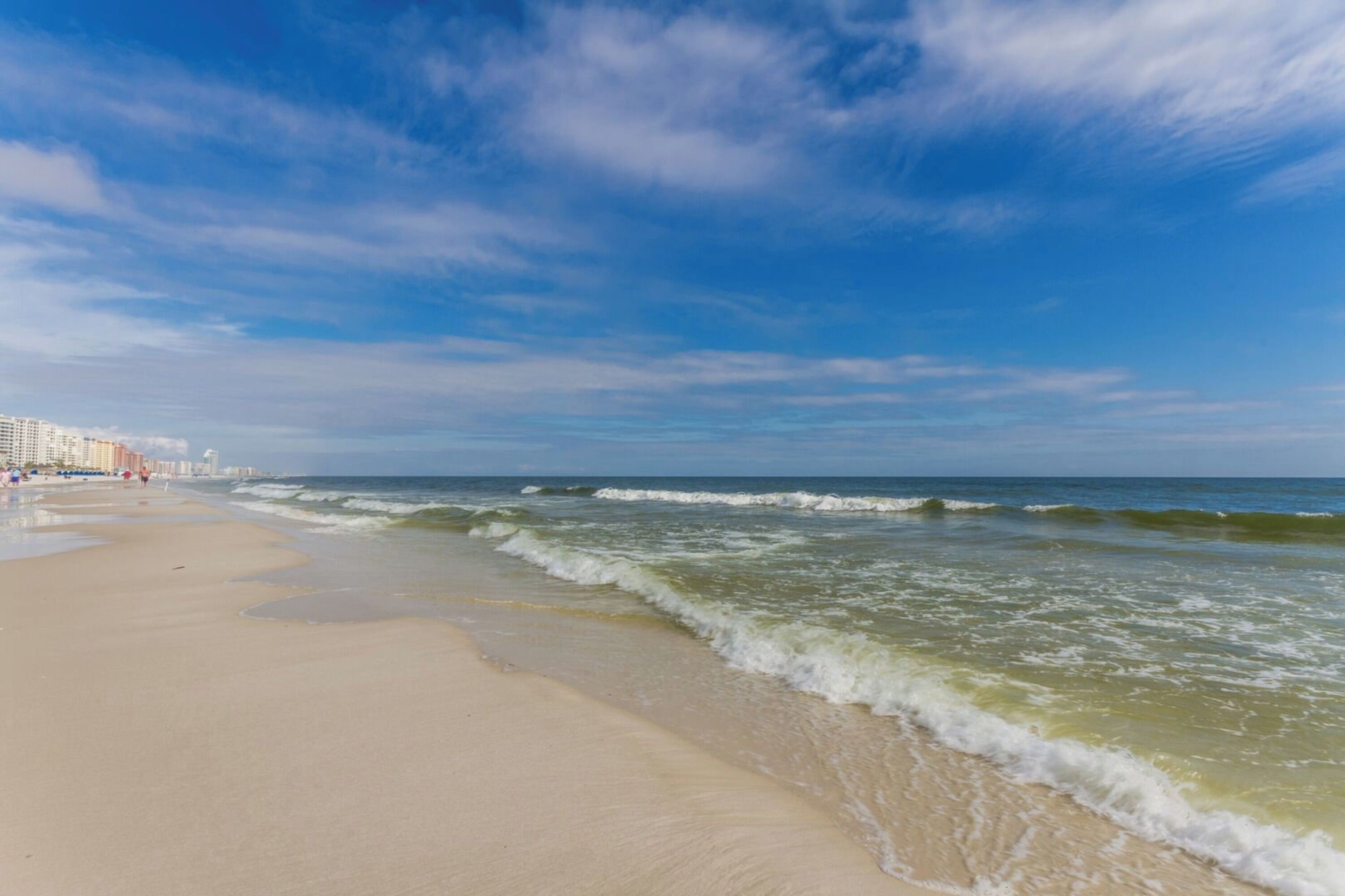A beach with waves, a clear sky, and buildings in the background.