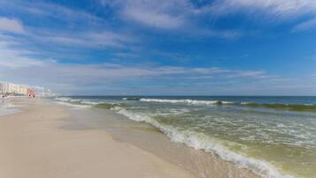 A beach with waves, a clear sky, and buildings in the background.