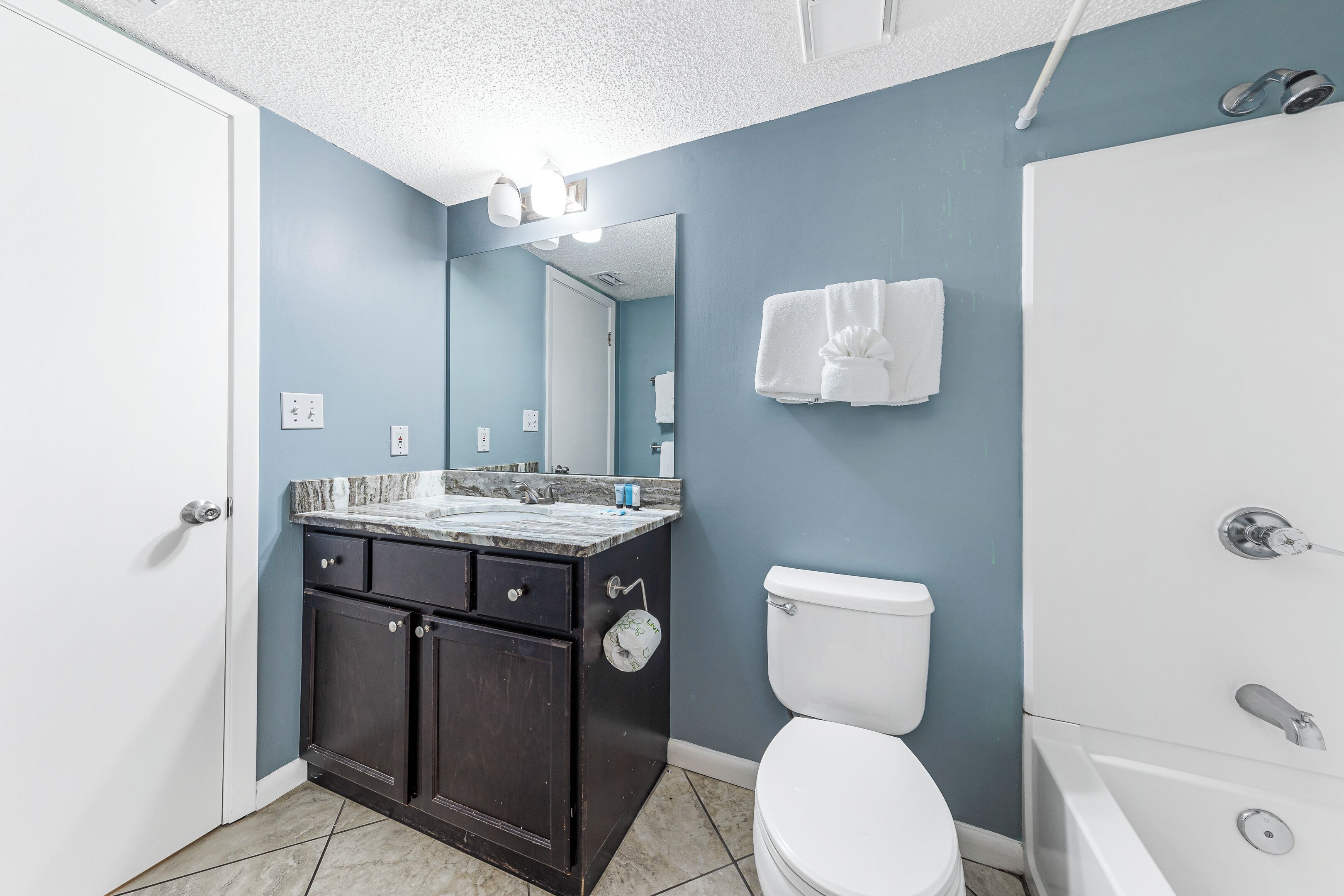 A bathroom with a white toilet, a dark wooden vanity with a marble countertop, and a white bathtub.