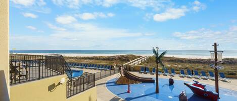 A pool area with a slide and lounge chairs, overlooking the beach.