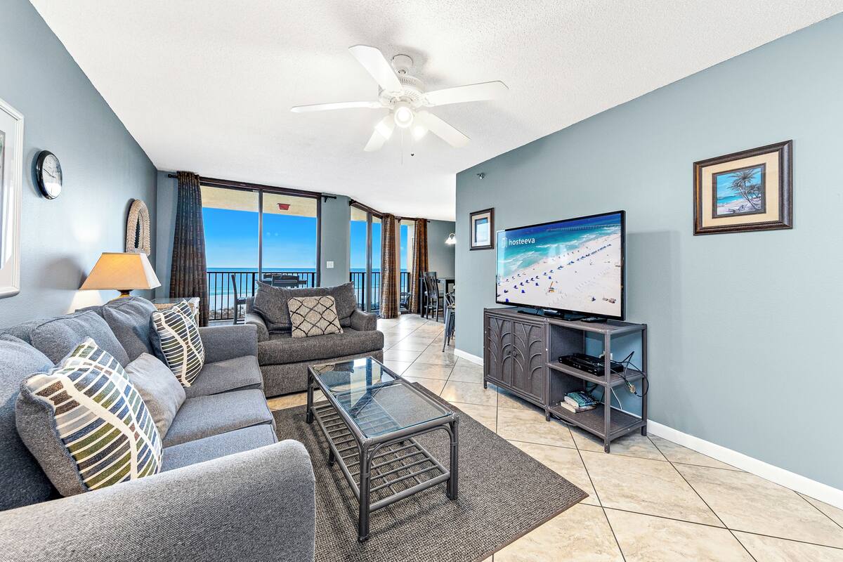 Una sala de estar con sofá, mesa de centro, televisor y vista a la playa.