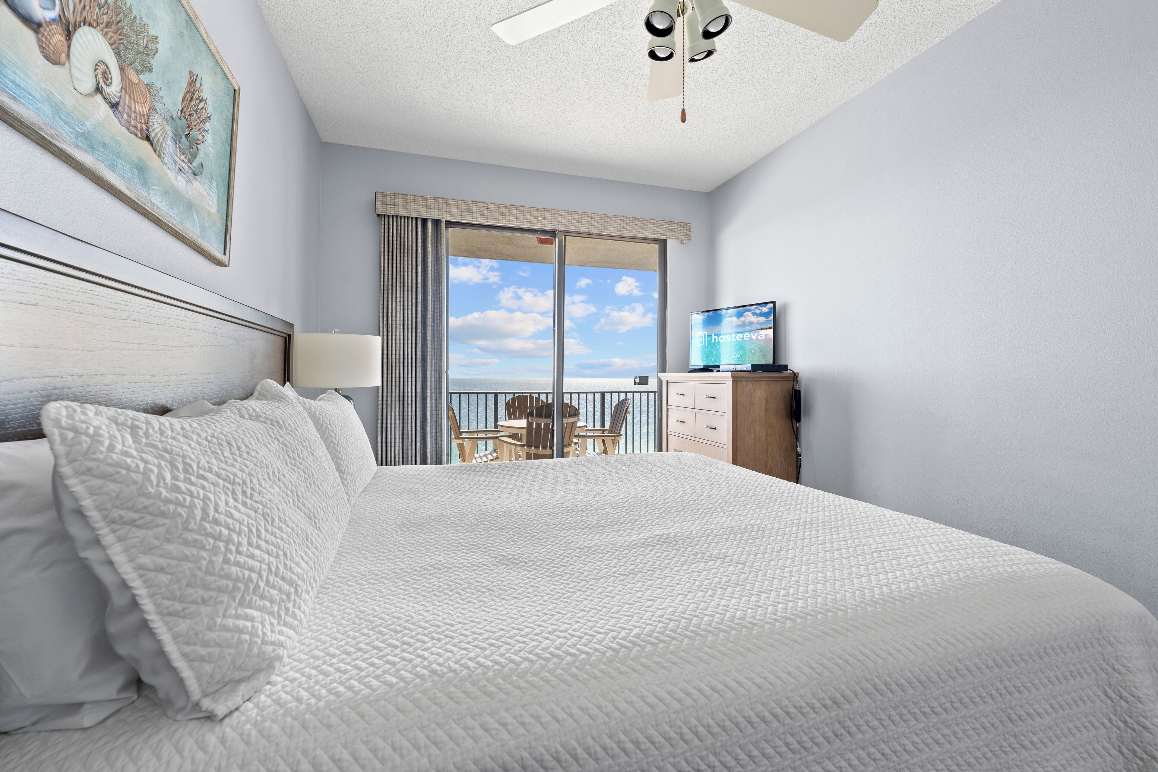 A hotel room with a large bed, a television, a desk, and a view of the sky through the window.