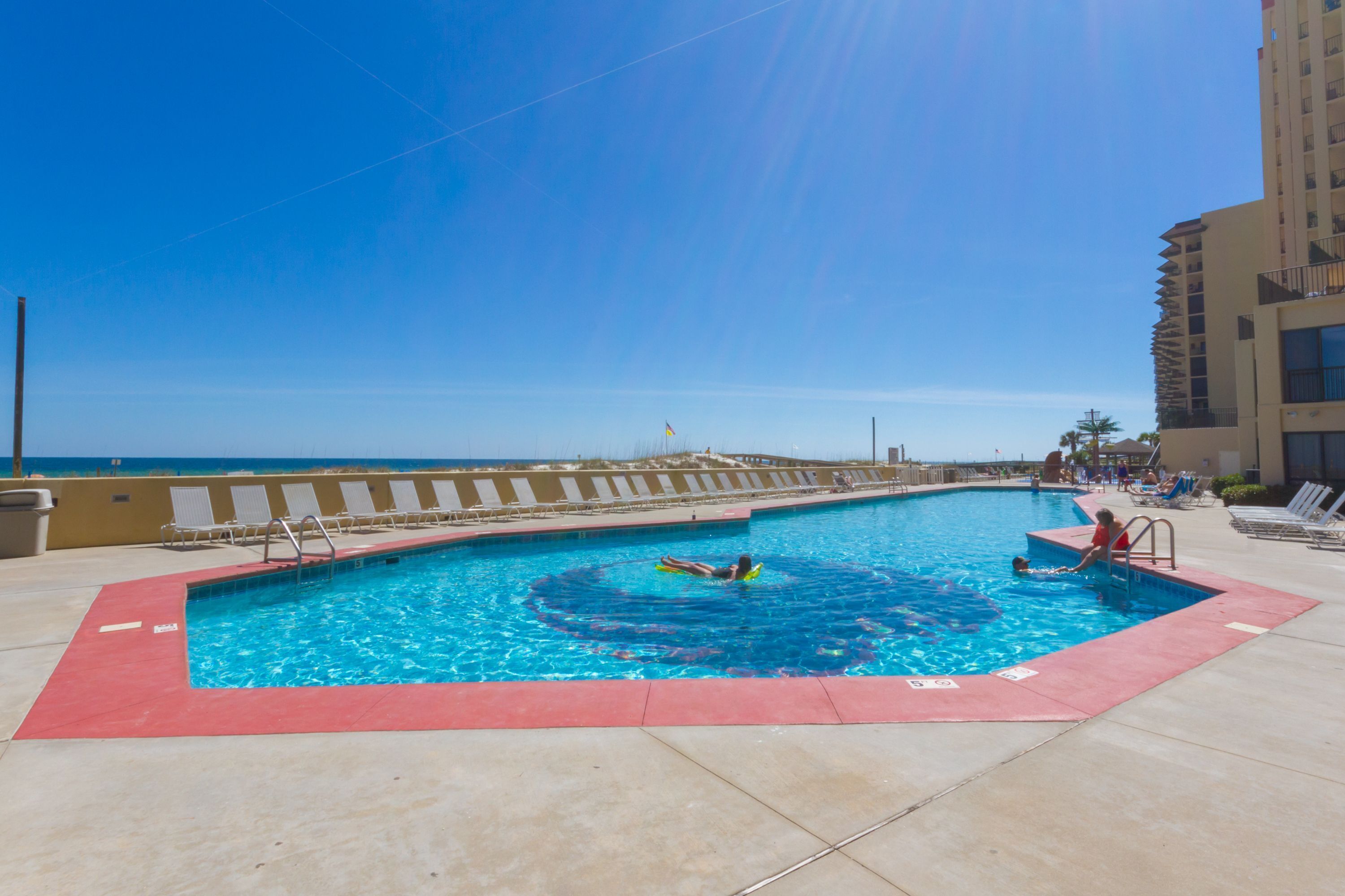 A swimming pool with a red border, a lifeguard chair, and a view of the ocean.