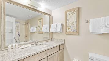 A bathroom with a large mirror, two sinks, wooden cabinets, and a toilet.