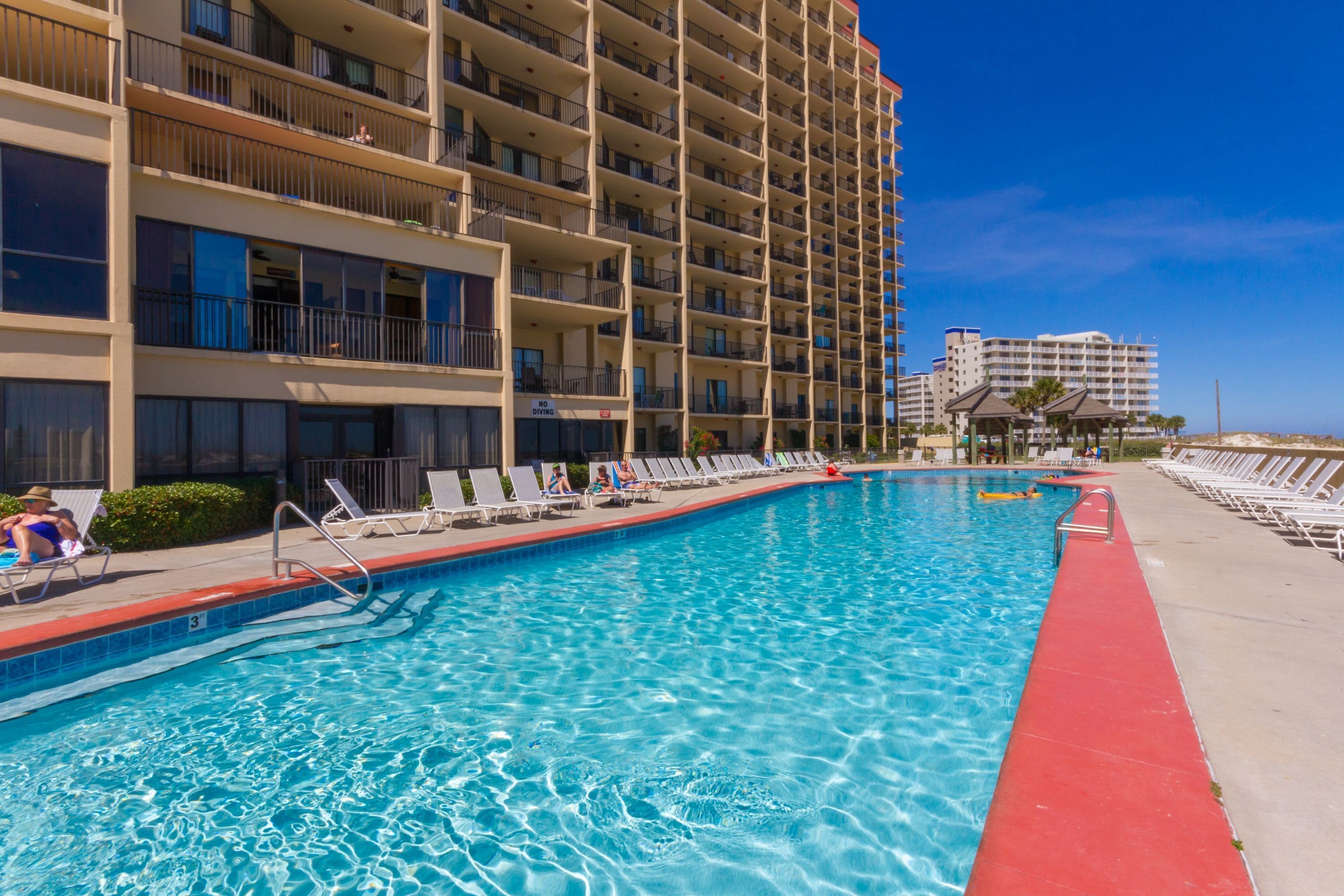 A hotel pool with sun loungers and a building with multiple balconies.