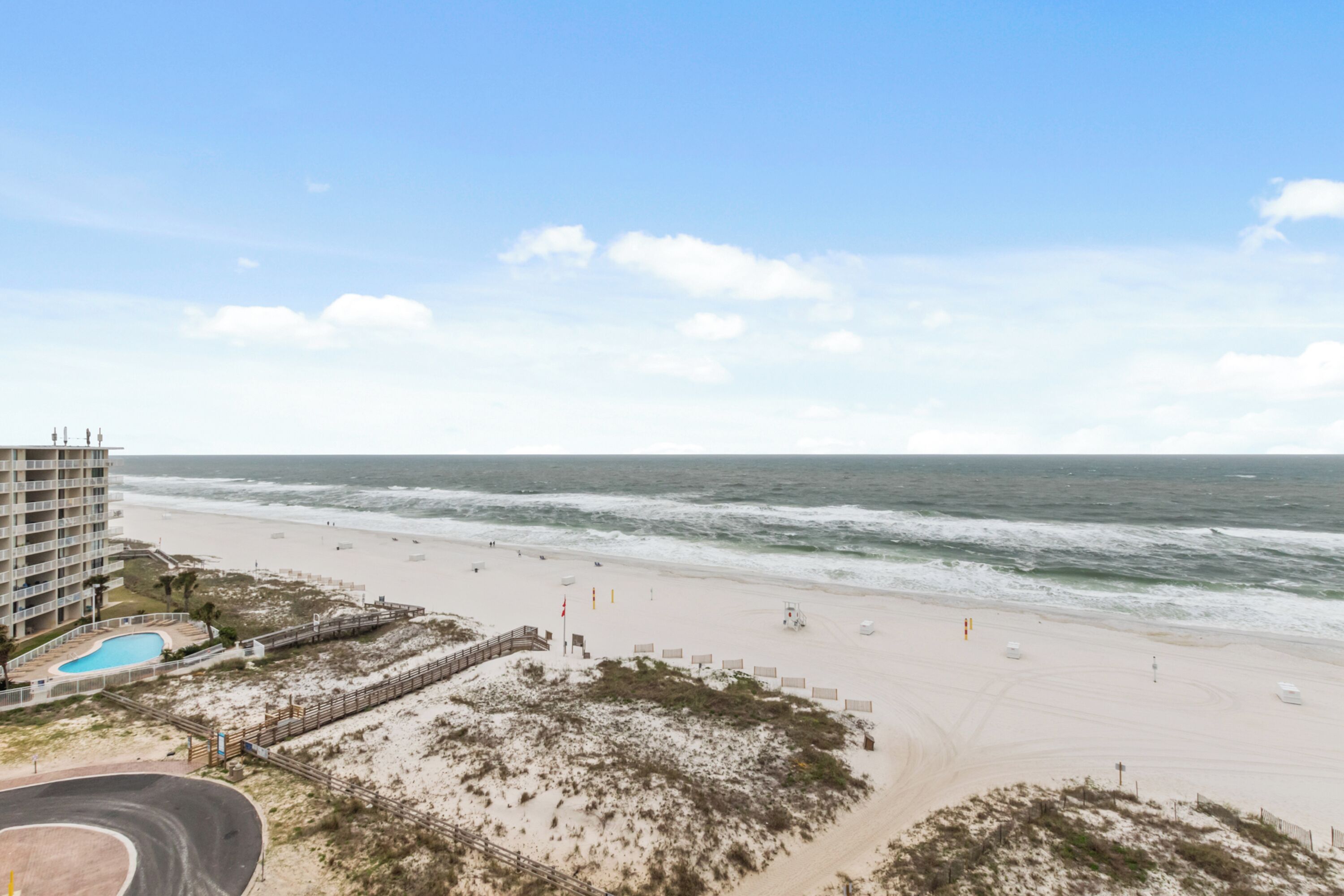 A beach with a hotel in the background, a clear sky, and the ocean.