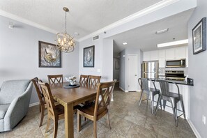 A dining area with a wooden table and chairs, a chandelier, and artwork on the walls. - Phoenix V Vacation Rental Condominiums (Orange Beach)