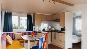 Une cuisine de taille réduite avec des meubles en bois, une table à manger entourée de chaises colorées et une fenêtre agrémentée de rideaux.