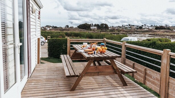 Une terrasse en bois avec une table de pique-nique, offrant une vue sur un paysage côtier.