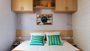 Un lit avec deux oreillers, une tête de lit en bois, une étagère au-dessus du lit et un tableau encadré accroché au mur.