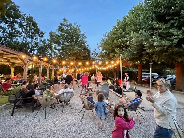 Un espace extérieur aménagé en terrasse, avec des tables et des chaises, des guirlandes lumineuses et des arbres en arrière-plan.