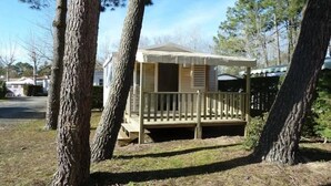 A small, single-story mobile home with a porch and a covered area, surrounded by trees.