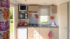 A compact kitchen with a microwave, stove, sink, and a small refrigerator.