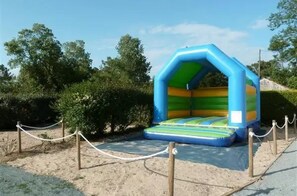 Un castillo inflable con interior verde y azul, rodeado por una barrera de cuerda y árboles.