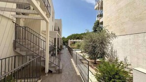 Un étroit sentier bordé de bâtiments dotés de balcons et d’un petit arbre.
