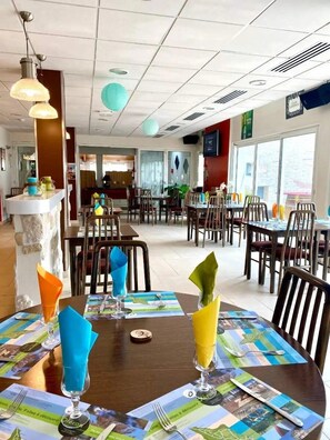 A restaurant with multiple tables, each set with a placemat, napkin, and glass.