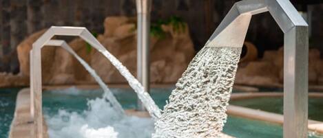 Un élément décoratif aquatique composé de deux structures métalliques d’où jaillit de l’eau qui se déverse dans un bassin.