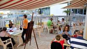 Un área de comedor al aire libre con mesas y sillas, un caballete de madera y vistas a una piscina y un edificio al fondo.