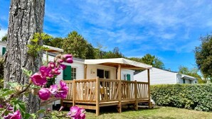 Una casa móvil con un porche y una pequeña terraza, rodeada de follaje y árboles.