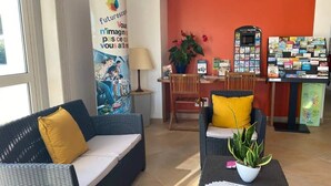 Un área de recepción con mobiliario de mimbre, una planta sobre una mesa, un cartel y un expositor de folletos.