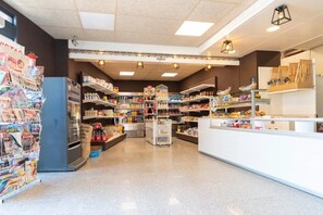 Interior de una tienda de comestibles con estantes llenos de diversos productos, una sección refrigerada y una zona de cajas.