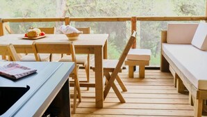 Een houten terras met een tafel, stoelen, een bankje en een bijzettafeltje met een mand en een ananas.