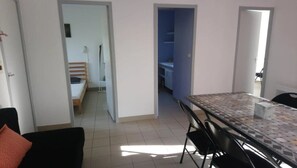 Une pièce avec un sol carrelé, une table à manger avec des chaises, et une vue sur un couloir menant à une autre pièce.