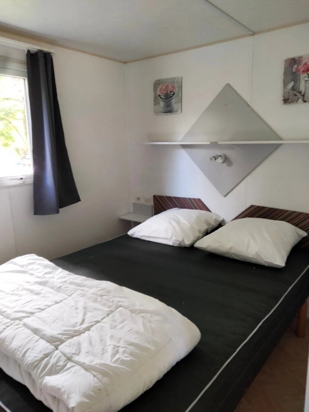 A single bed with white bedding, a dark mattress, and a headboard with a mirror.