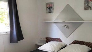 En enkeltseng med hvidt sengetøj, en mørk madras og en sengegavl med et spejl.