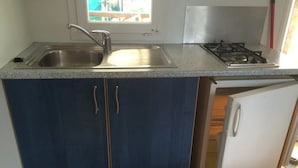 A kitchen with a stainless steel sink, a gas stove, and a white refrigerator. - ZEcamping 3 étoiles chiens acceptés mobil-home 21m2 4 pers (Auxonne)
