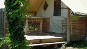Eine zeltartige Konstruktion mit einer Holzterrasse, einem kleinen Tisch und einem Stuhl.