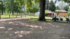 A gravel area with a tree, a wooden fence, and a building with a red roof. - ZEcamping 3* dog friendly mobil-home 16m2 2 pers (Auxonne)