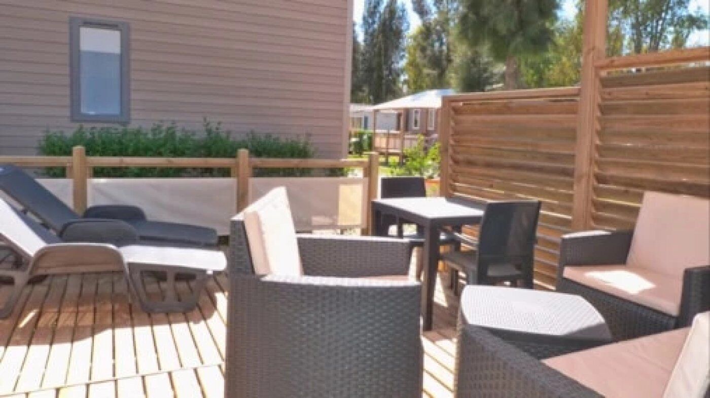 Un espace patio aménagé avec des meubles en osier, notamment des chaises et une table, et une clôture en bois.
