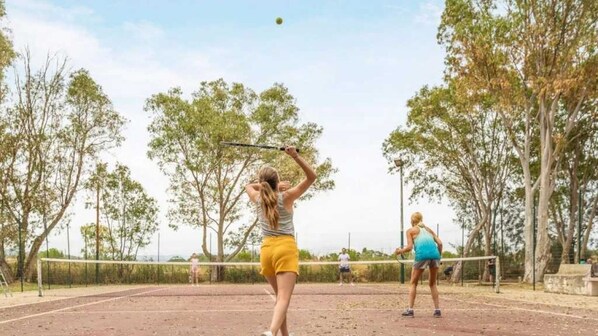 An outdoor tennis court with a net in the middle, surrounded by trees.