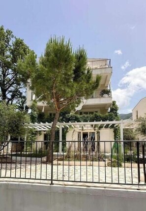 A multi-story building with balconies, surrounded by trees and a paved area.